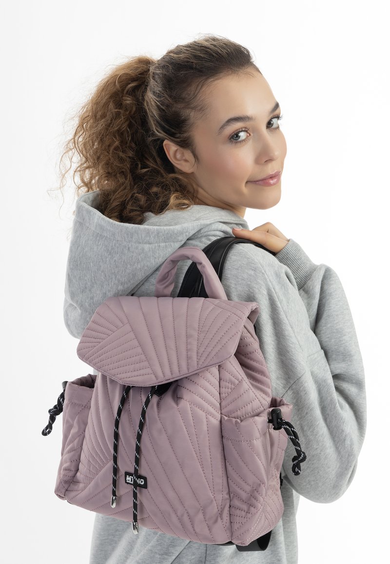 Zaino rosa trapuntato con pattina, dotato di lacci neri e tasche. Materiale morbido con un motivo geometrico sulla parte esterna.