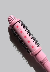 Brosse de coiffage chauffante rose avec un manche texturé, des poils noirs et des points d'indicateur rouges le long du tube. Design cylindrique pour le coiffage des cheveux.