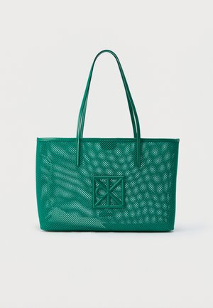 Sac fourre-tout en cuir vert avec un design perforé et un patch logo géométrique, comprenant deux bretelles, sur un fond uni.