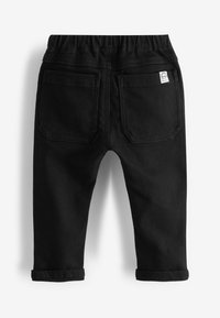 Pantalon noir pour tout-petit avec taille élastique, deux poches arrière, revers roulés et petite étiquette blanche en tissu avec logo sur la poche droite.
