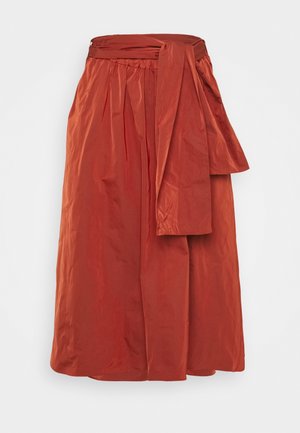 Jupe midi couleur rouille avec une taille froncée et une large ceinture en tissu nouée sur le côté.