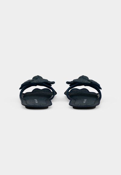 Par mørkeblå slip-on sandaler med stoffsløyfer på frontstroppene, sett bakfra mot en ensfarget lys bakgrunn.