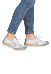 Les baskets légères présentent un design en matériaux mixtes avec des accents bleus, des motifs floraux, et une semelle intermédiaire en liège texturée. Fermeture à lacets avec une fermeture éclair latérale.