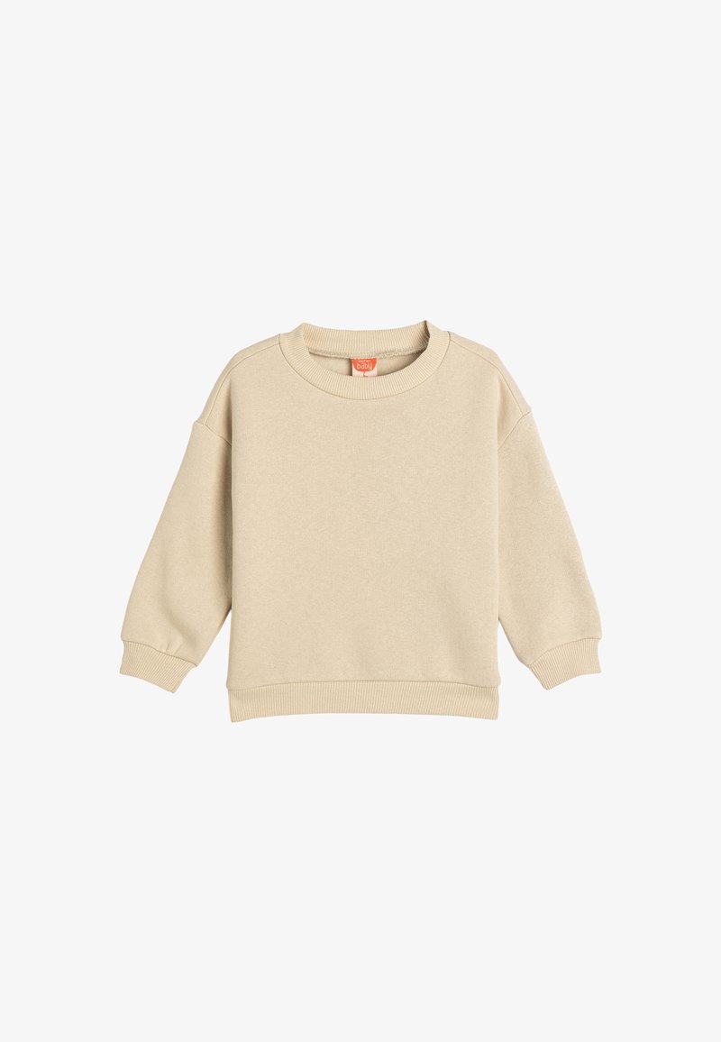 Beige huppari, joka on valmistettu pehmeästä kankaasta, pyöreällä kaula-aukolla, pudotetuilla hartioilla sekä ribbaillut hihansuut ja helma. Ei näkyviä kuvioita tai lisäkoristuksia.