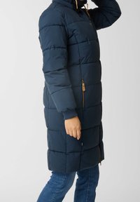 Manteau rembourré bleu marine avec des coutures horizontales, fermeture éclair intégrale, poches latérales et capuche. Détails marron sur la fermeture éclair et les poignets.