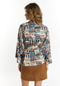 Blusa multicolore con design a peplum, caratterizzata da una stampa di forme astratte in blu, arancione e nero su uno sfondo chiaro. Maniche lunghe.