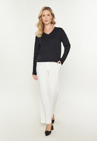 Pulover negru cu decolteu în V, pantaloni largi albi și pantofi cu toc înalt negri. Texturi netede cu un design ușor și clasic.