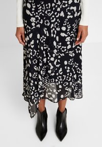 Jupe midi imprimée animal en noir et blanc, fabriquée en tissu léger, avec un design fluide et une fente latérale haute, associée à des bottines noires.