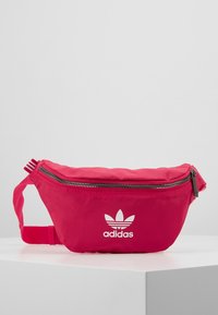 Rosa ryggsäck med en slät nylonfinish, med en zippered stängning, justerbar rem och vit Adidas-logotyp på framsidan.