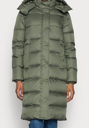 Long manteau d’hiver matelassé vert olive avec boutons-pression, poches latérales et capuche amovible, porté sur un jean bleu.