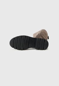 Botte cheville en daim marron avec un bout arrondi, fermeture éclair et une semelle en caoutchouc noire texturée présentant des rainures horizontales pour une meilleure adhérence.