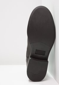Semelle en caoutchouc noir avec une texture lisse, marquée "GUESS" à l'arrière. Design élégant et épuré, adapté à une tenue formelle ou décontractée.