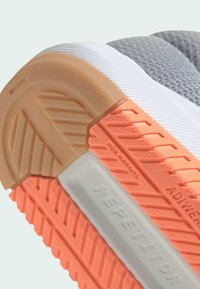 Zbliżenie na podeszwę trampka z beżowymi, koralowymi i białymi sekcjami bieżnika, pokazujące teksturę non-marking i ADIWEAR, zapewniającą przyczepność i trwałość.