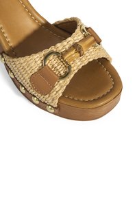 Gewebte Strohwedge-Sandale mit braunen Lederelementen, Holzplattform, goldenen Nieten entlang der Kante und dekorativem Bambus-Schnallendetail.