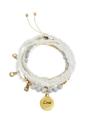 Stacked white beaded bracelets with gold accents and charms, including a round gold pendant engraved with the word "Love."