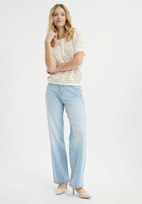 Haut en tricot crème avec des rayures texturées, associé à un jean droit bleu clair et des chaussures à talons nus. Ensemble simple et décontracté.