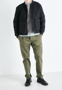 Zwarte gewatteerde bomberjack met drukknoopsluiting, grijze sweatshirt, gestreept shirt, olijfgroene broek en zwarte sneakers. Eenvoudig, textuur ontwerp.