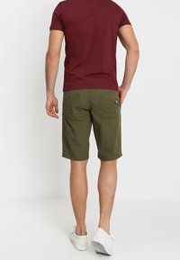 Shorts cargo vert olive en coton, dotés de deux poches arrière et d'une coupe classique. Comprend un patch logo sur la ceinture.