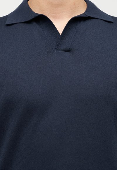 Πουκάμισο πόλο σε ναυτικό μπλε χρώμα, κατασκευασμένο από υφασμάτινη υφή, με κοντό γιακά και v-λαιμόκοψη. Χωρίς ορατά μοτίβα ή μεταλλικά στοιχεία.