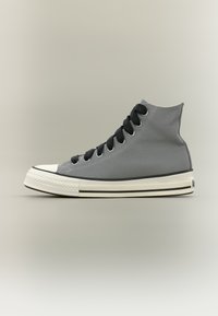 Grå høy-toppsneaker med svarte snøringer, hvit gummitåhette og hvit såle med svarte striper på en nøytral bakgrunn.