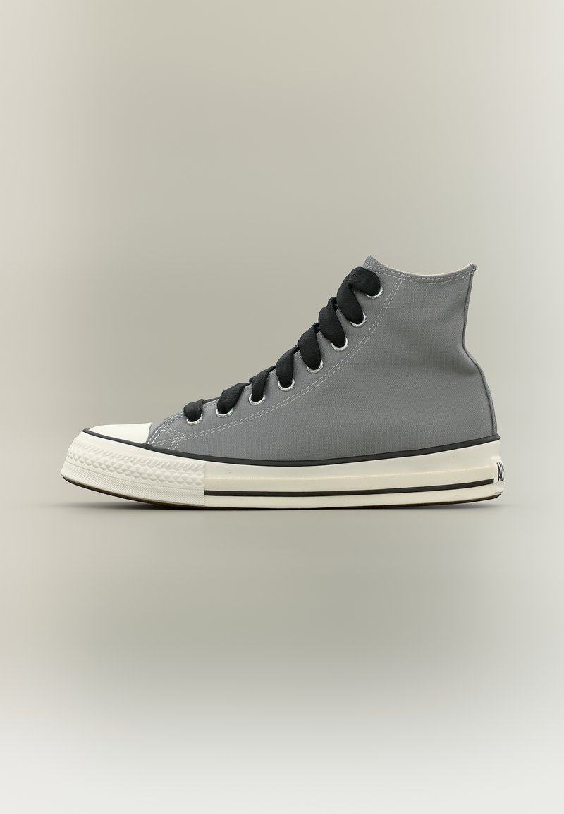 Sneaker grigio con punta alta, lacci neri, punta in gomma bianca e suola bianca con strisce nere su sfondo neutro.