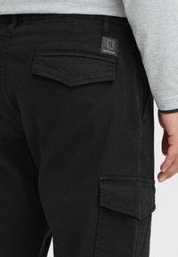 Black cargo pants made of durable fabric, featuring side pockets, a back pocket with stitching details, and a small logo tag.