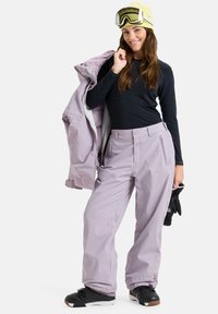 Snow pants in light lavender, featuring a relaxed fit, zippered pockets, and durable, water-resistant material. Paired with a black top and jacket.