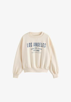 Helebeige dressipluus puhvvarrukatega, soonikkoesed ja ribaga äär. Sinine tekst: "LOS ANGELES CHAMPIONS LEAGUE EST.1982."