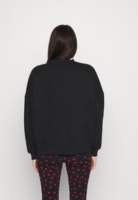Sudadera negra de gran tamaño con hombros caídos, combinada con leggings negros ajustados con un patrón de corazones rojos. Textura suave, diseño casual.