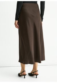 Brown satin midi skirt with a smooth texture, a sleek silhouette, and a subtle flare at the bottom, paired with black heeled sandals.