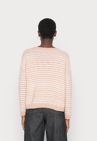 Jasnoróżowy sweter w paski o luźnym kroju, z szerokimi rękawami i ściągaczem u dołu. Posiada poziome białe paski oraz miękką, dzianinową strukturę.