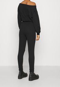 Sudadera negra sin hombros combinada con leggings negros, con un diseño ajustado y puños acanalados en los tobillos, usada con botas negras gruesas.