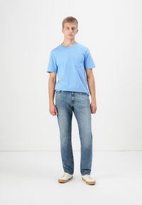 Kék pamut póló rövid ujjakkal és mellzsebbel, világoskék farmernadrággal és bézs sportcipővel párosítva. Egyszerű dizájn és illeszkedés.