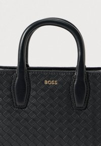 Czarna skórzana torebka o plecionej fakturze, z zaokrąglonymi uchwytami i złotym akcentem logo "BOSS". Kompaktowy design zapewniający wszechstronne zastosowanie.