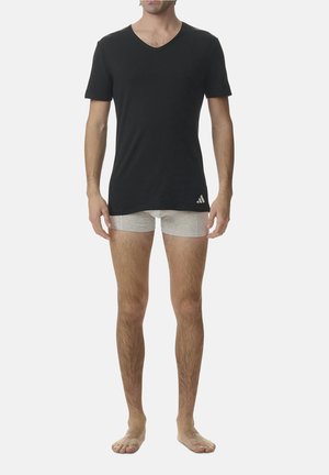 Schwarzes kurzärmliges V-Ausschnitt-T-Shirt mit grauem Logo, kombiniert mit hellgrauen Boxershorts. Das Modell ist barfuß vor einem schlichten Hintergrund.