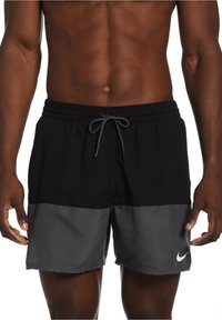 Pantaloni da nuoto Nike neri e grigi con vita elasticizzata, chiusura con lacci e logo bianco sulla gamba sinistra. Tessuto leggero.