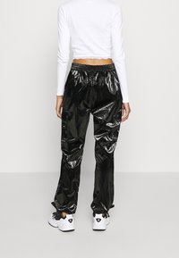 Black shiny track pants with a loose fit and elastic waistband, featuring side pockets and elastic cuffs, paired with white sneakers.