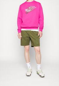 Pink Nike sweatshirt with logo, paired with olive green cargo shorts featuring a side pocket. Worn with white and green athletic shoes.