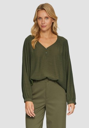 Blouse vert olive avec un décolleté en V et des manches longues. Caractéristiques de boutons décoratifs et d'un tissu texturé, associée à un pantalon assorti.