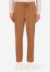 Pantaloni in maglia marrone con vita regolabile, caratterizzati da dettagli sulle cuciture laterali e un fit rilassato, abbinati a sneaker bianche.