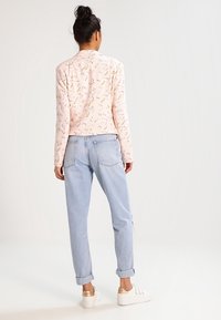 Lys rosa sweater med blomsterprint, parret med lyseblå, kort jeans. Modellen har hvid sneakers med gyldne detaljer på.