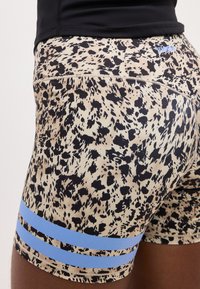 Αθλητικά σορτς με τύπωμα λεοπάρδαλης και δύο μπλε ρίγες στο μπούτι, φορεμένα με μαύρο τοπ, που δείχνουν την πλευρική και πίσω όψη.