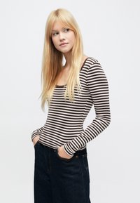 Hosszú ujjú, barna és krémszínű csíkos top, szélesített nyakkivágással és testre szabott fazonnal. Sötét színű, magas derekú farmerral párosítva.