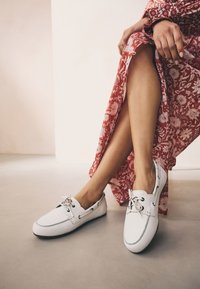 Hvide læderbådsko med sorte øjer, grå syninger og snøre. Kombineret med en rød kjole med blomsterprint.