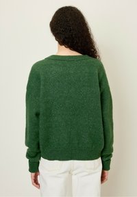 Maglione verde in un morbido filato testurizzato. Caratterizzato da una vestibilità rilassata, polsini e orlo a coste. Vista dal retro che mostra un ampio scollo e una silhouette morbida.