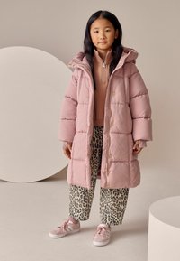 Lyserød pufferjakke med hætte, lynlås foran og gyldent hardware; parret med leopardprintbukser og lyserøde sneakers. Overordnet glat tekstur.