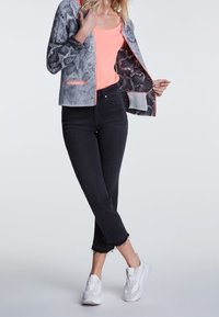 Veste à imprimé serpent gris avec des accents rose fluo sur un débardeur rose, associés à un jean noir court et des baskets blanches.