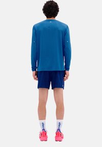Langärmliges blaues Sporthemd, marineblaue Shorts, rosa Laufschuhe und weiße Socken mit blauen Akzenten. Glatter Stoff und athletische Passform.