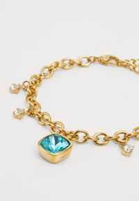 Bracciale in catena d'oro con una grande pietra quadrata di turchese e tre piccole cristalli trasparenti incastonati in impostazioni color oro.