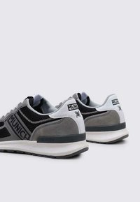 Zapatilla negra y gris con materiales de malla y ante. Presenta un refuerzo en el talón blanco y la marca "MUNICH" en gris. Suela de goma, diseño moderno.